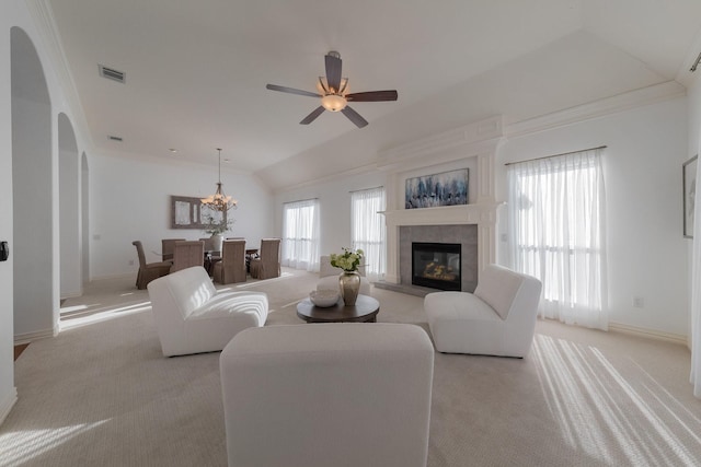 living room with lofted ceiling, ceiling fan with notable chandelier, a tiled fireplace, ornamental molding, and light carpet