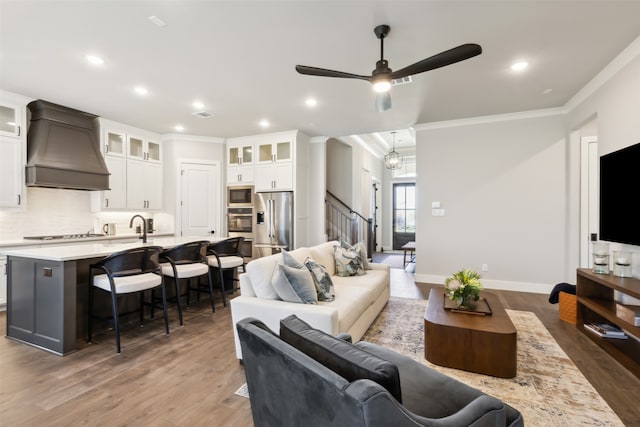 living room with dark wood-type flooring, ceiling fan with notable chandelier, and ornamental molding