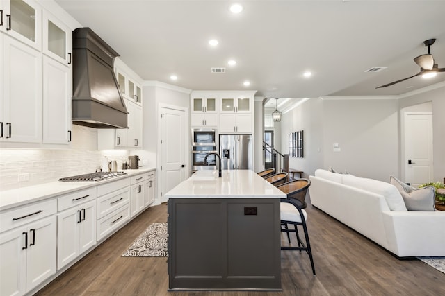 kitchen featuring dark hardwood / wood-style flooring, custom range hood, stainless steel appliances, ceiling fan, and a center island with sink