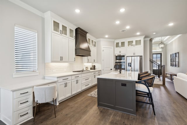 kitchen with stainless steel appliances, a kitchen bar, a center island with sink, custom exhaust hood, and ornamental molding