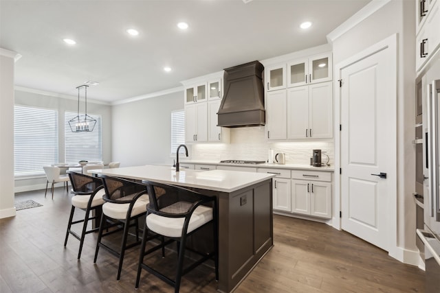 kitchen with hanging light fixtures, white cabinetry, a kitchen island with sink, and custom exhaust hood