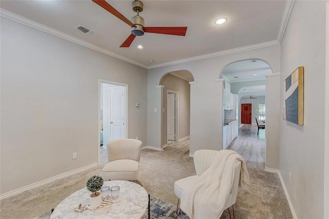 living area with crown molding, ceiling fan, and light colored carpet