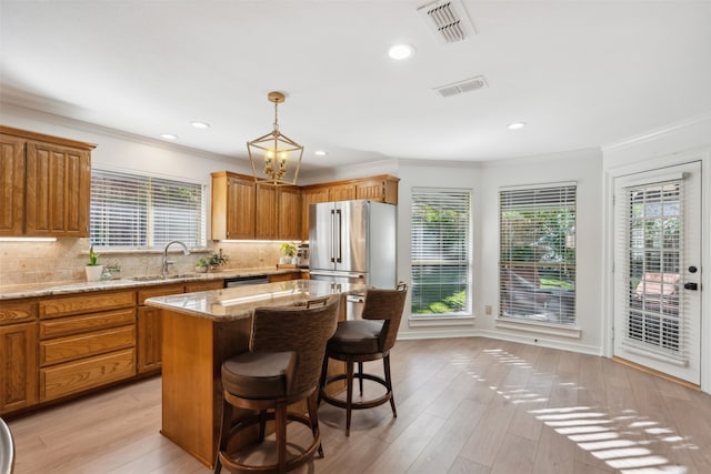 kitchen with backsplash, stainless steel appliances, sink, light hardwood / wood-style flooring, and a center island