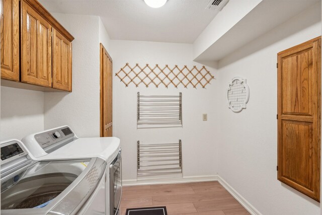 laundry room with cabinets, light wood-type flooring, and separate washer and dryer