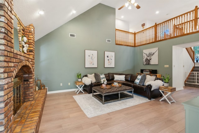 living room with ceiling fan, a fireplace, high vaulted ceiling, and light hardwood / wood-style floors