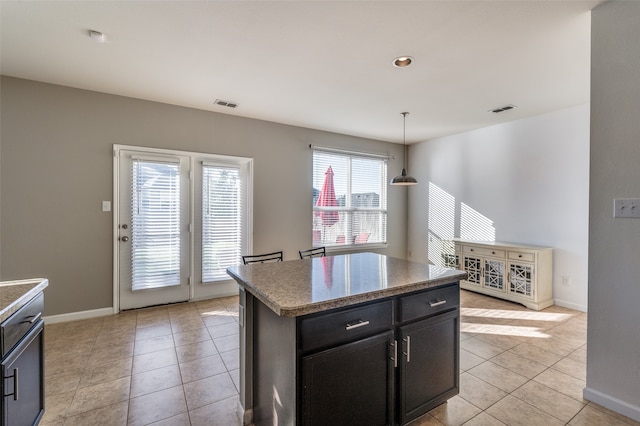 kitchen with a center island, light tile patterned flooring, light stone countertops, and hanging light fixtures