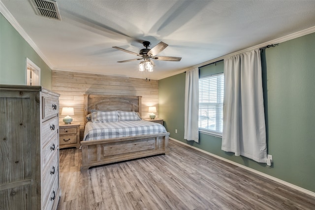 bedroom featuring ceiling fan, wood walls, light wood-type flooring, and ornamental molding