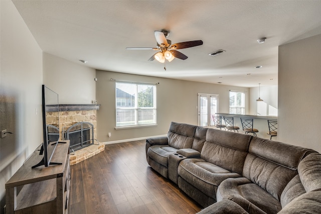 living room with dark hardwood / wood-style floors, a stone fireplace, a wealth of natural light, and ceiling fan