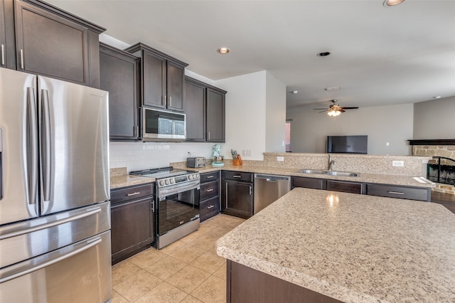 kitchen with a stone fireplace, sink, ceiling fan, dark brown cabinets, and stainless steel appliances