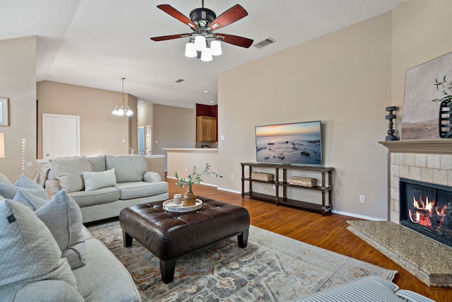 living room with a textured ceiling, lofted ceiling, a fireplace, ceiling fan with notable chandelier, and hardwood / wood-style flooring