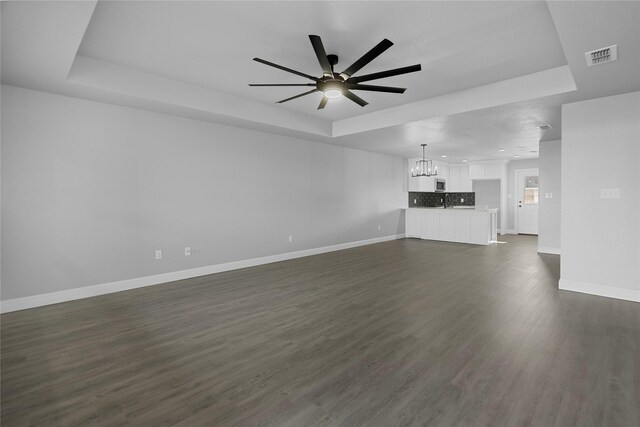 unfurnished living room with ceiling fan with notable chandelier, dark hardwood / wood-style flooring, and a tray ceiling