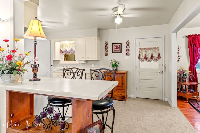 kitchen featuring a kitchen breakfast bar, kitchen peninsula, light hardwood / wood-style flooring, ceiling fan, and white cabinetry