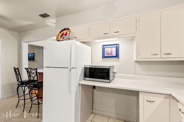 kitchen featuring light tile patterned floors, white refrigerator, and white cabinetry