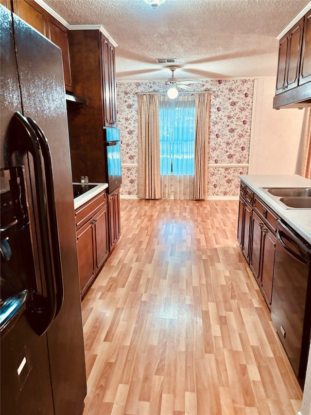 kitchen featuring black appliances, sink, light wood-type flooring, and a textured ceiling