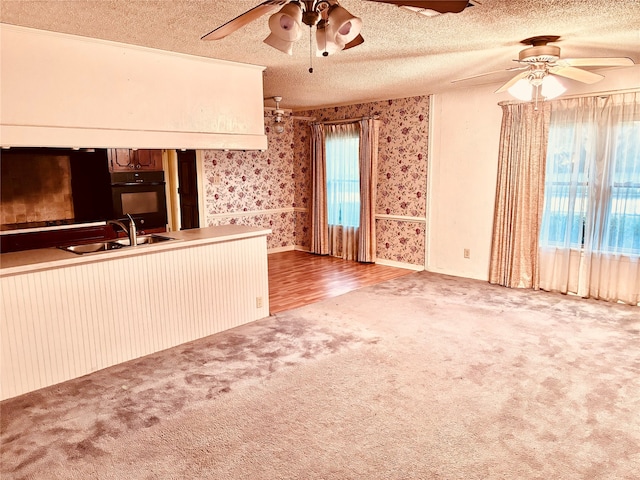 unfurnished living room featuring a textured ceiling, ceiling fan, light colored carpet, and sink