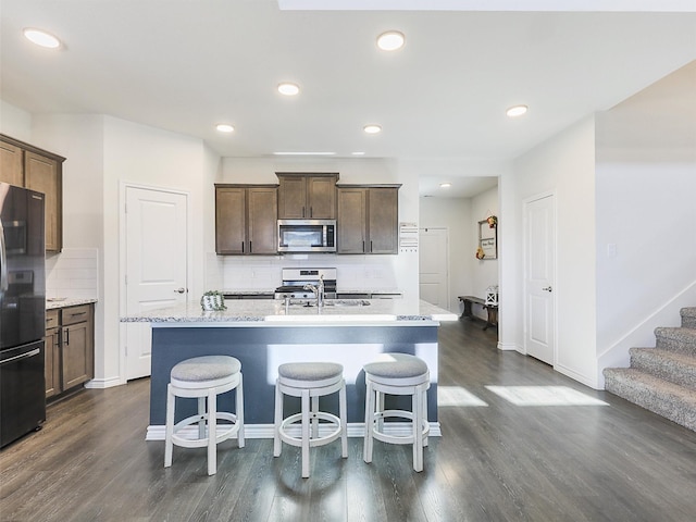 1013 Saddle Club Way, Princeton, TX 75407 - kitchen featuring appliances with stainless steel finishes, backsplash, dark wood-style floors, an island with sink, and a breakfast bar area