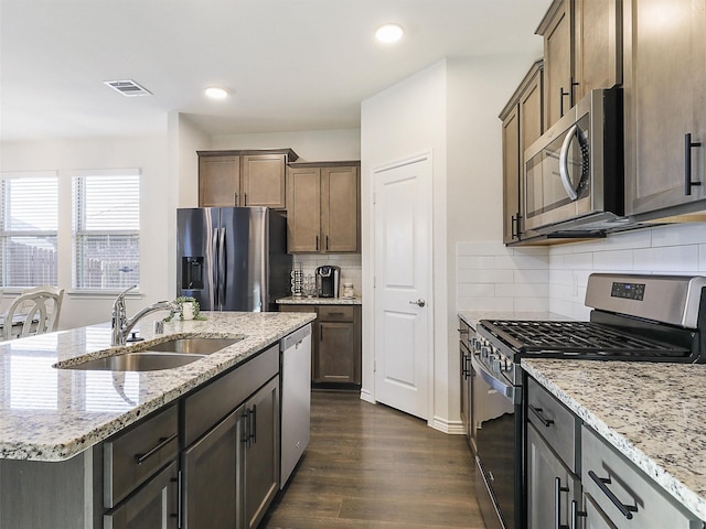 kitchen with light stone countertops, sink, stainless steel appliances, dark hardwood / wood-style floors, and a center island with sink