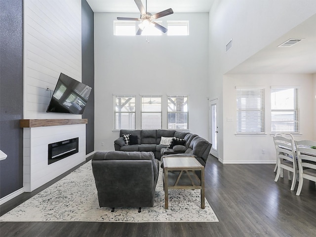 living room with ceiling fan, a large fireplace, a high ceiling, and dark hardwood / wood-style floors