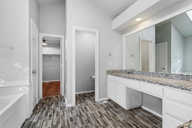 bathroom featuring a bath, wood-type flooring, a textured ceiling, vaulted ceiling, and vanity