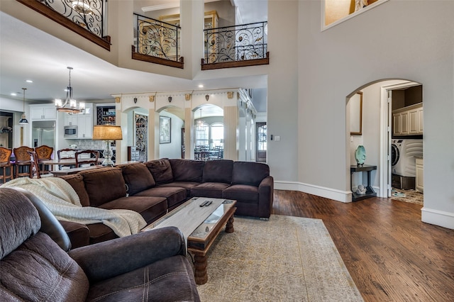 living room with a towering ceiling, dark hardwood / wood-style floors, washer / clothes dryer, and a notable chandelier