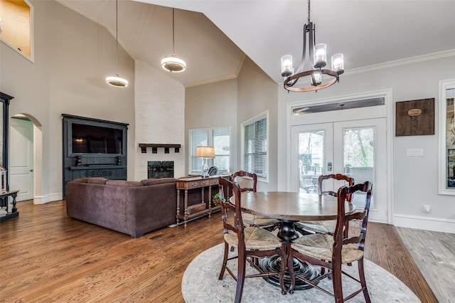 dining room featuring a large fireplace, a towering ceiling, wood-type flooring, and ornamental molding