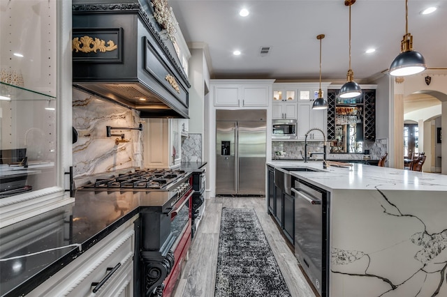 kitchen with light wood-type flooring, dark stone counters, built in appliances, white cabinets, and hanging light fixtures