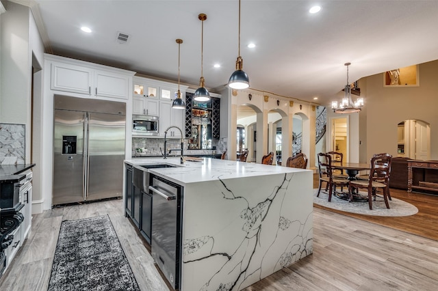 kitchen featuring light wood-type flooring, built in appliances, white cabinetry, hanging light fixtures, and a large island