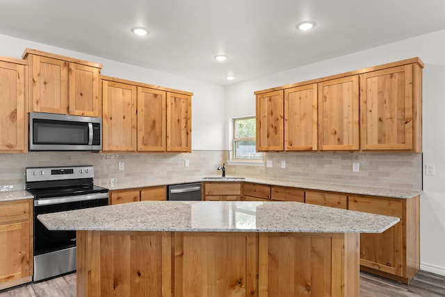 kitchen with light stone countertops, a kitchen island, light hardwood / wood-style floors, and appliances with stainless steel finishes