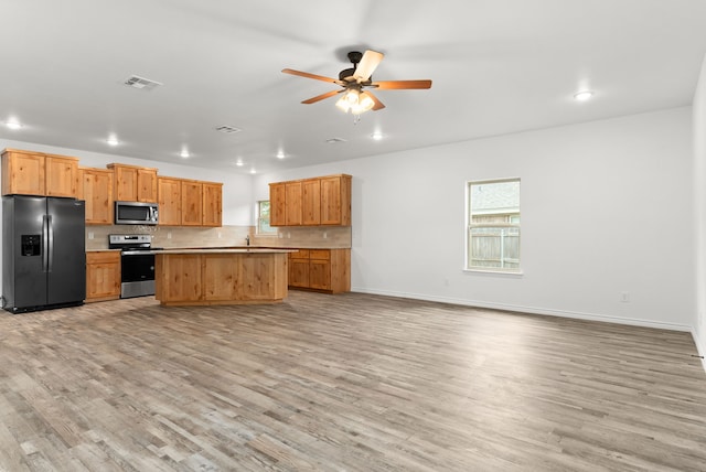 kitchen featuring ceiling fan, a kitchen island, appliances with stainless steel finishes, tasteful backsplash, and light hardwood / wood-style floors