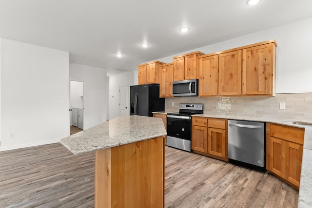 kitchen with a center island, light stone counters, light hardwood / wood-style flooring, backsplash, and appliances with stainless steel finishes