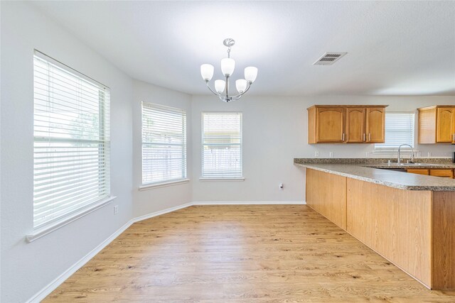 kitchen with an inviting chandelier, hanging light fixtures, a wealth of natural light, light hardwood / wood-style floors, and kitchen peninsula