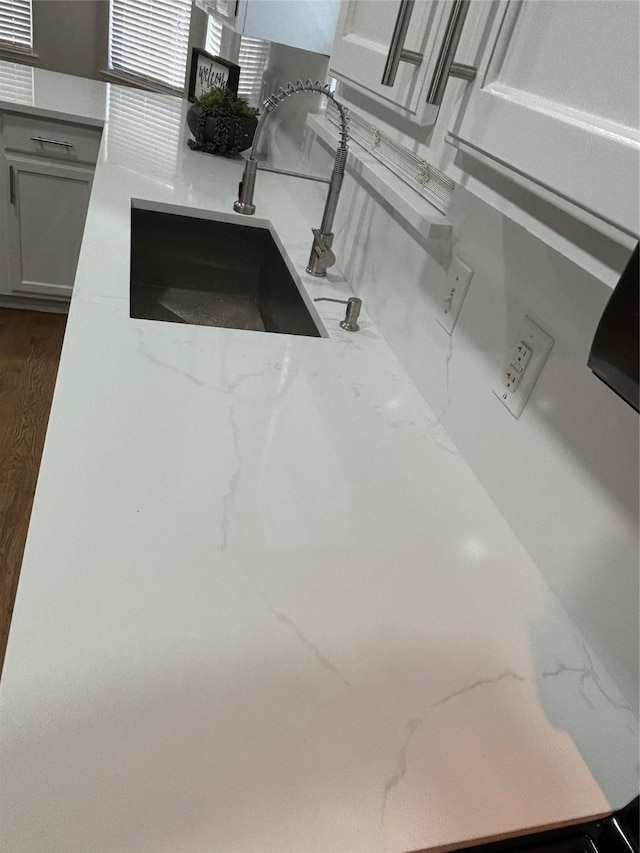 interior details featuring light stone countertops, sink, and white cabinets