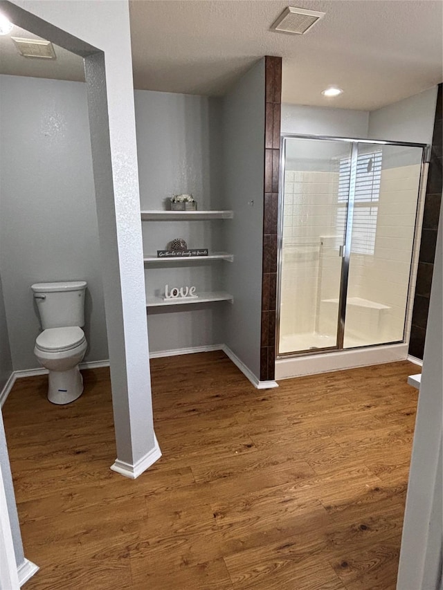 bathroom with a textured ceiling, wood-type flooring, a shower with door, and toilet