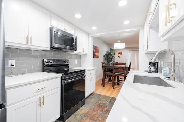 kitchen featuring electric range, sink, white cabinets, and pendant lighting