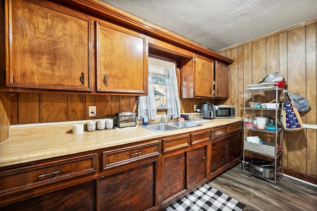 kitchen featuring a textured ceiling, wooden walls, sink, and dark hardwood / wood-style floors