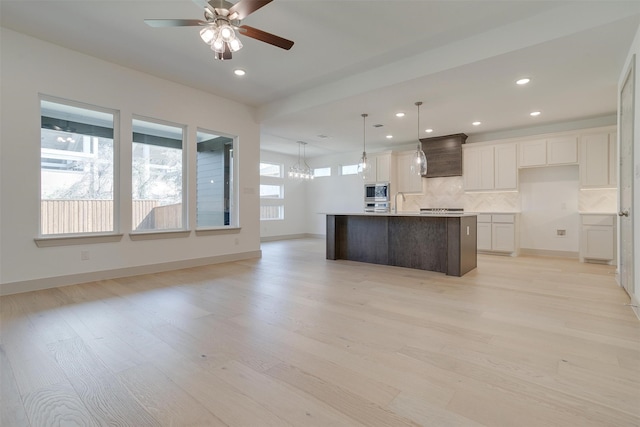 kitchen featuring pendant lighting, backsplash, stainless steel appliances, white cabinets, and a center island with sink