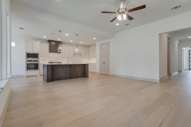 kitchen featuring built in microwave, oven, a kitchen island with sink, and pendant lighting