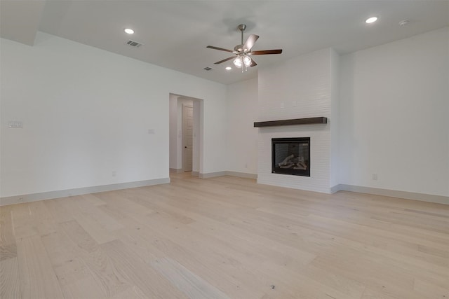 unfurnished living room featuring light hardwood / wood-style flooring, a large fireplace, and ceiling fan