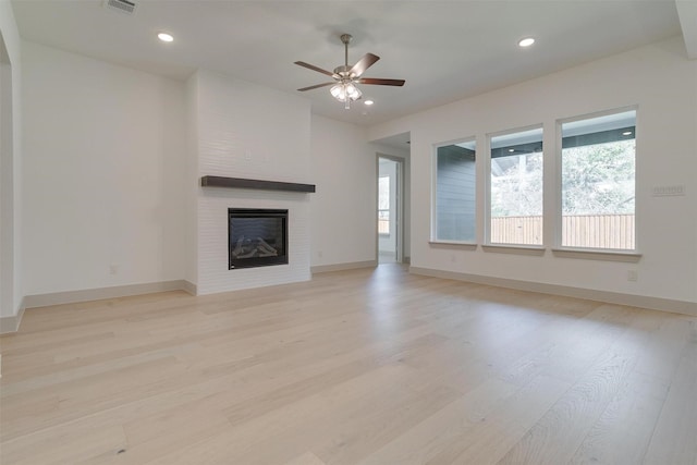 unfurnished living room featuring ceiling fan, a fireplace, and light hardwood / wood-style flooring