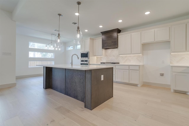 kitchen featuring a kitchen island with sink, decorative light fixtures, tasteful backsplash, and white cabinets