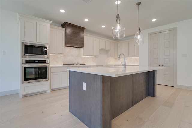 kitchen featuring white cabinetry, oven, a kitchen island with sink, and built in microwave