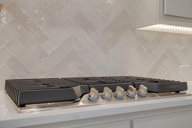 room details featuring stainless steel gas stovetop, white cabinets, and decorative backsplash