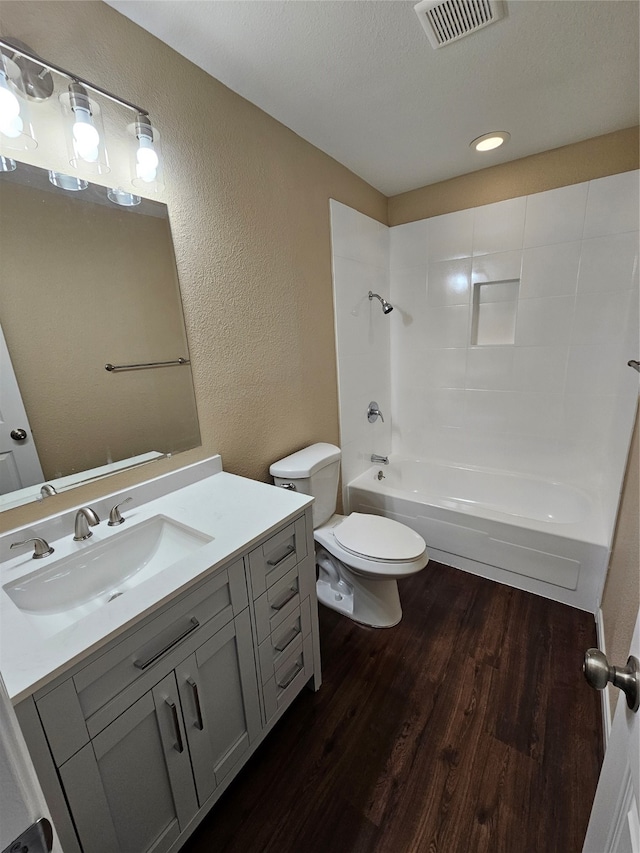 full bathroom with washtub / shower combination, hardwood / wood-style floors, a textured ceiling, toilet, and vanity