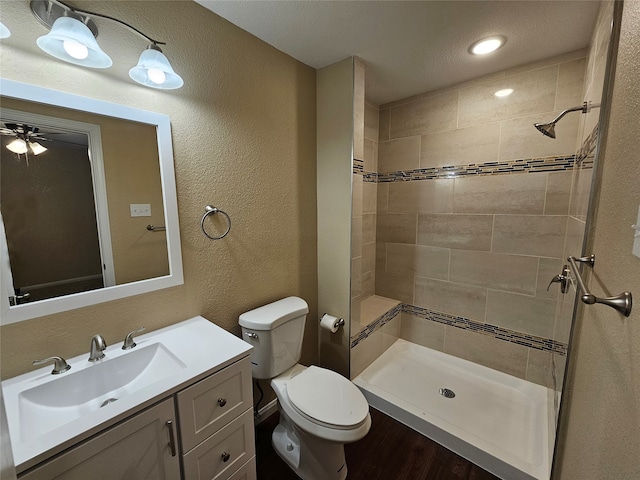 bathroom with a tile shower, ceiling fan, a textured ceiling, toilet, and vanity