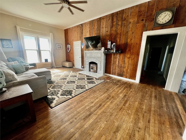 living room featuring ceiling fan, wood walls, crown molding, wood-type flooring, and a fireplace