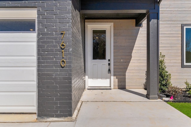 entrance to property featuring a garage and brick siding