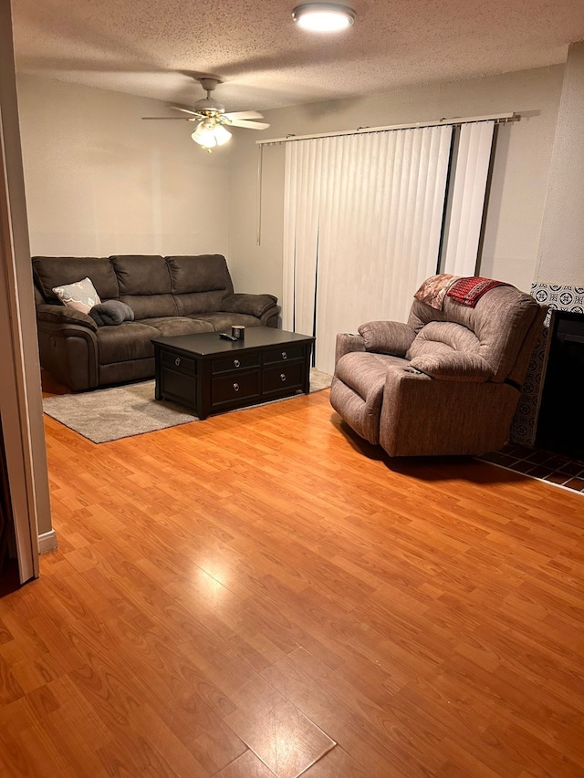 living room featuring ceiling fan, light hardwood / wood-style floors, and a textured ceiling