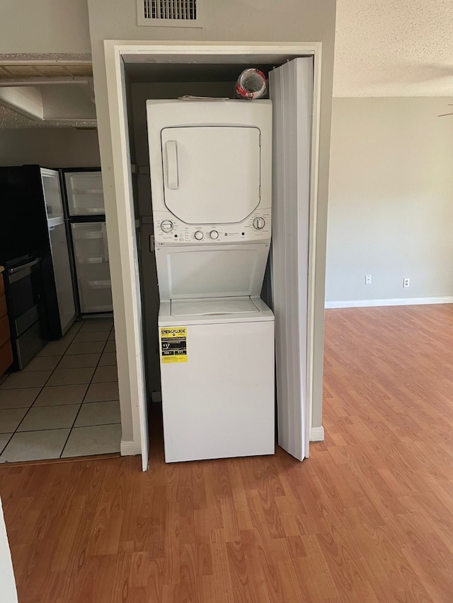 clothes washing area with light hardwood / wood-style floors and stacked washer / drying machine