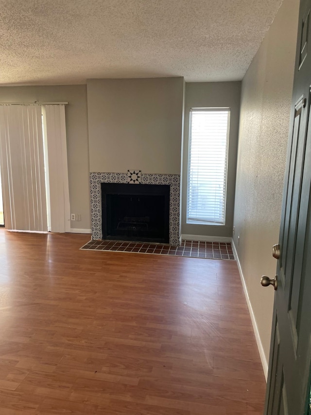 unfurnished living room featuring a textured ceiling, dark hardwood / wood-style flooring, and a tiled fireplace