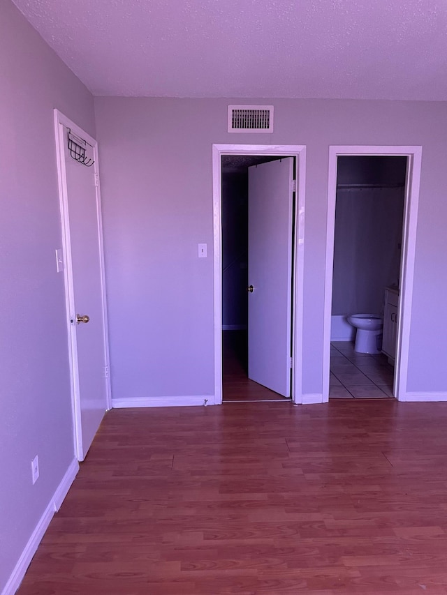 unfurnished bedroom featuring hardwood / wood-style flooring, a spacious closet, a closet, and ensuite bathroom